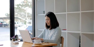 年轻女子在图书馆用笔记本电脑工作，喝着热咖啡