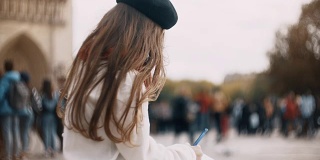 一个漂亮的小女孩拿着笔记本坐在法国巴黎圣母院附近画素描