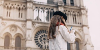 小艺术家贝雷帽在巴黎圣母院附近，法国。时髦女孩在著名的教堂附近做她的爱好