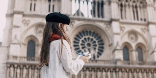 戴着黑色贝雷帽和红色围巾的小艺术家在笔记本上画画，在法国巴黎圣母院附近，著名的大教堂