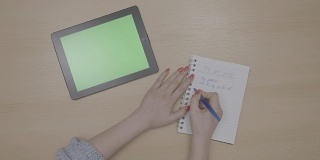 俯视图的女人手计划做清单与绿色屏幕平板电脑和书写在记事本上