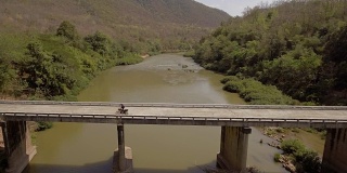 航拍冒险摩托车骑在横跨泰国南省南河的一座桥上俯视图