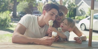 有爱的年轻家庭在公园吃甜筒冰淇淋。爸爸舔了舔儿子的蛋筒，递给他