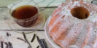 老式的沙蛋糕，一杯红茶和几片香草在木制的背景。蛋黄海绵蛋糕，草莓在乡村白色的背景