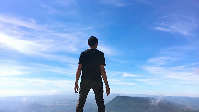 一个人站在山上，手臂举得很慢。蓝天和白云