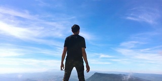 一个人站在山上，手臂举得很慢。蓝天和白云