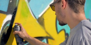 涂鸦艺术家正在墙上黄色字母附近画一条黑线。