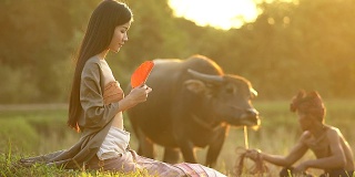 美丽的亚洲女人的肖像坐在傍晚与温暖的照明日落的田野。