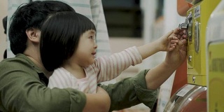 亚洲的父亲和女儿正在用玩具机买玩具旁边的母亲-家庭购物与休闲活动