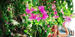 年轻美丽的女人走在粉红色的花的花园里，触摸和闻花和微笑。缓慢的运动。1920 x1080