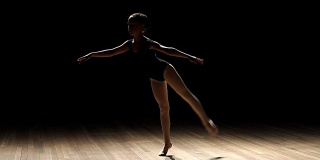 一个年轻的芭蕾舞者在黑色背景上摆姿势。