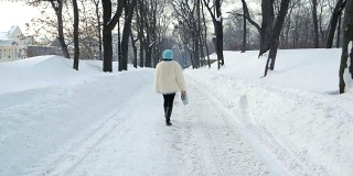 穿着白色毛皮大衣的漂亮女人在公园里散步。它正在下雪。缓慢的运动。冬季森林。时尚的女孩独自一人