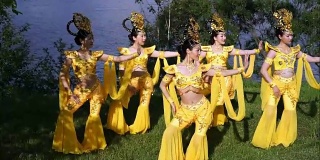 五名亚洲女演员穿着中国传统的黄色服装在河边跳着美丽的舞蹈
