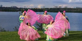 五名亚洲女演员身着中国传统服饰，与粉丝们一起在河边跳舞