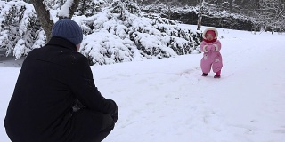 在寒冷的冬天，爸爸和宝宝在白雪覆盖的公园里玩耍。FullHD