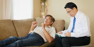 沮丧的亚洲老年人躺在沙发上看精神病医生检查