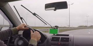 智能手机与绿色空白屏幕在汽车上的方向，按摩，位置。现代汽车和智能手机的绿屏司机。色度键。男人在阴雨天开车。下雨了。业务。