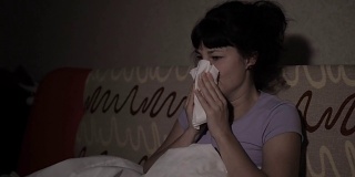 一个生病的女人晚上在家里的沙发上打喷嚏。女孩流鼻涕，拿纸巾，流感症状。医疗保健和医疗理念。感冒是流感的感染。