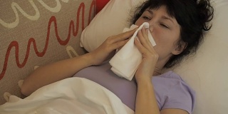一个生病的女人坐在家里的沙发上打喷嚏。女孩流鼻涕，拿纸巾，流感症状。医疗保健和医疗理念。感冒是流感的感染。