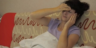 一位年轻女子正遭受着严重的头痛。感冒发烧。生病的女孩躺在沙发上，盖着毯子，用手摸着自己的头。