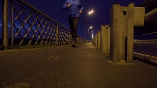 晚上在桥边慢跑的运动员。一个穿着运动服的男人在晚上跑步。男正在健身，车路过。视频素材模板下载