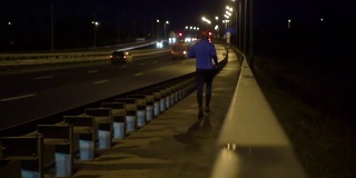 晚上在桥边慢跑的运动员。一个穿着运动服的男人在晚上跑步。男正在健身，车路过。