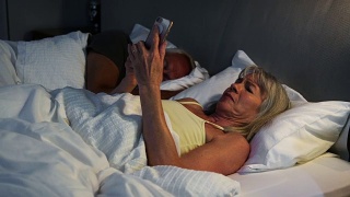 夜不能寐的老年妇女在床上使用手机视频素材模板下载