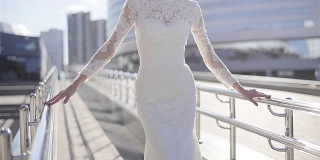 女人在优雅的白色长蕾丝设计连衣裙摆姿势在阳光明媚的城市背景春天快乐。新娘在城市街道上近距离展示昂贵的服装。婚纱时装设计师服装