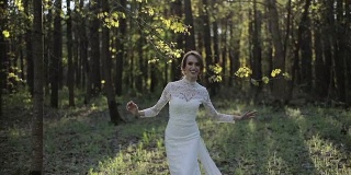 优雅的少女，穿着白色蕾丝长裙，走在春天的森林里，抚摸着藏在树枝后面的树叶。新娘穿着节日的衣服礼服站在绿色新鲜的树林微笑情绪幸福的生活