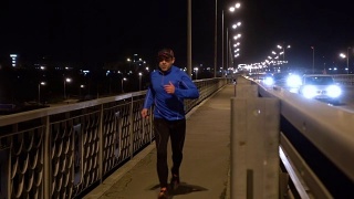 晚上在桥边慢跑的运动员。一个穿着运动服的男人在晚上跑步。男正在健身，车路过。傍晚沿着高速公路慢跑。视频素材模板下载