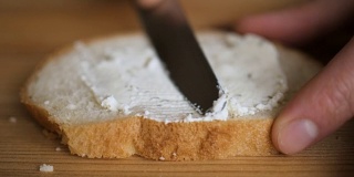 一个男人用一把刀在黑麦烤面包上涂黄油。把奶油涂在面包上的人。男性的双手在厨房的面包上涂抹黄油，慢镜头。
