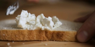 一个男人用一把刀在黑麦烤面包上涂黄油。把奶油涂在面包上的人。男性的双手在厨房的面包上涂抹黄油，慢镜头。