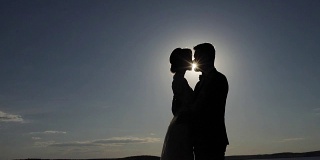剪影情侣在爱拥抱和享受亲密的时刻一起天空背景对比阴影傍晚太阳照耀光束。男人背光女人抱着对方亲吻拷贝空间。相信爱