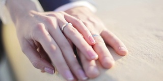 男女双手用结婚戒指拉近，握着互相抚摸，阳光的光线模糊了背景，景深浅。指甲油艺术家大师。新娘忠诚家庭联系统一理念