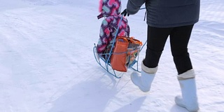 一个女人在冬天和一个小女孩推着雪橇