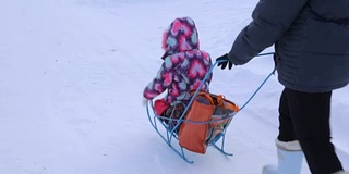 一个女人在冬天和一个小女孩推着雪橇