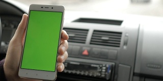 一只手拿着一个绿色空白屏幕的智能手机在车里为方向，按摩，位置，业务。男人坐在现代汽车里，用智能手机工作——绿色屏幕——特写。色度键。