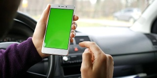 一只手拿着一个绿色空白屏幕的智能手机在车里为方向，按摩，位置，业务。男人坐在现代汽车里，用智能手机工作——绿色屏幕——特写。色度键。