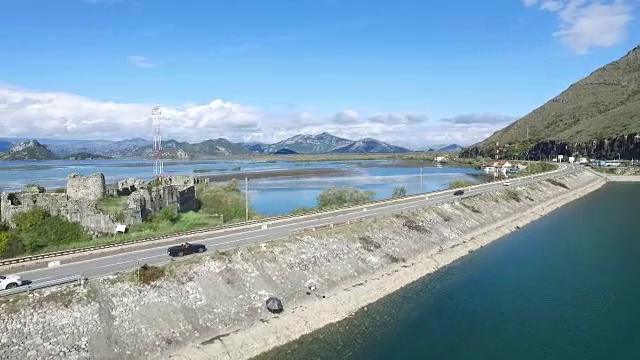 黑色的汽车在桥上行驶，蓝色的大海，群山和天空为背景。镜头。汽车在河边的路上行驶，鸟瞰图。镜头。鸟瞰图小森林湖及附近经过的公路