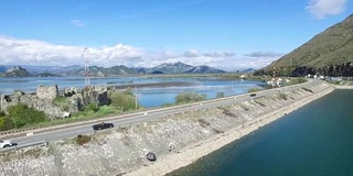 黑色的汽车在桥上行驶，蓝色的大海，群山和天空为背景。镜头。汽车在河边的路上行驶，鸟瞰图。镜头。鸟瞰图小森林湖及附近经过的公路