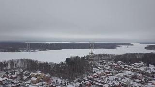 冬村鸟瞰图，河岸边有输电铁塔。冬季景观上的无人机输电塔和电力线视频素材模板下载