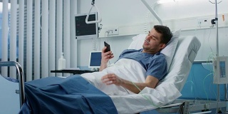 康复患者躺在医院病床上使用智能手机和微笑。友善的护士进来检查他。
