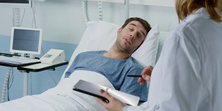 专业女医生看躺在床上的男病人，问他问题，用平板电脑填写病历。友好的卫生保健