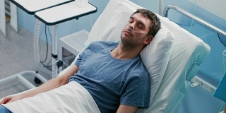 在医院生病的男性病人睡在床上，他戴着鼻导管。护士进来检查他的掉落计数器，增加止痛剂量。