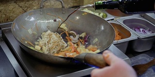 厨师将酱油和红烧酱倒入乌冬面和平底锅里炒的蔬菜中