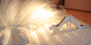 婚礼构图是躺在床上的时髦礼服和新娘的高跟鞋。鞋子之间的环。移动的阳光。