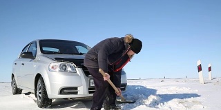 司机用铲子把汽车从雪中挖出来。