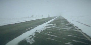 在大雪覆盖的西伯利亚路线上，汽车在一串卡车中行进，侧风阵阵