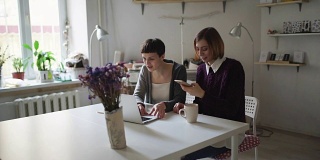 两个女性朋友坐在桌子边用笔记本打发闲暇时光