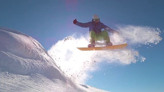 慢动作:专业滑雪板运动员在新雪中跳跃，向太阳喷洒雪花视频素材模板下载
